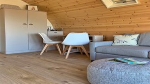 A cozy room with a wooden ceiling, a grey sofa, a white chair, a small table, and a cabinet.