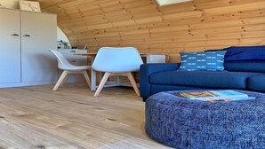 A cozy loft bedroom with a sloped ceiling, wooden beams, a white desk, a blue sofa, and a blue ottoman.