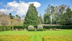 A well-manicured garden with a central pathway, neatly trimmed hedges, and a variety of trees. - Lodge in Thirsk with Spa & Scenic Trails (Thirsk)