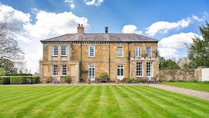 A large, two-story stone building with a symmetrical facade, large windows, and a well-maintained lawn in front.