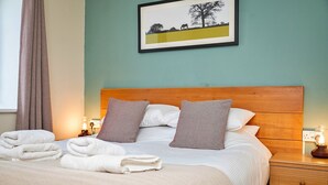A neatly made bed with white linens and two pillows, a wooden headboard, and a bedside table with a lamp. - Lodge in Thirsk with Spa & Scenic Trails (Thirsk)