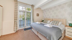 Une chambre à coucher avec un lit, une table de chevet et une vue sur l’extérieur par une fenêtre ornée de rideaux.