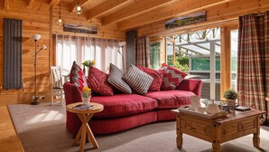 Interior acogedor de una cabaña de madera con un sofá rojo, una mesa de centro de madera y un amplio ventanal con cortinas.