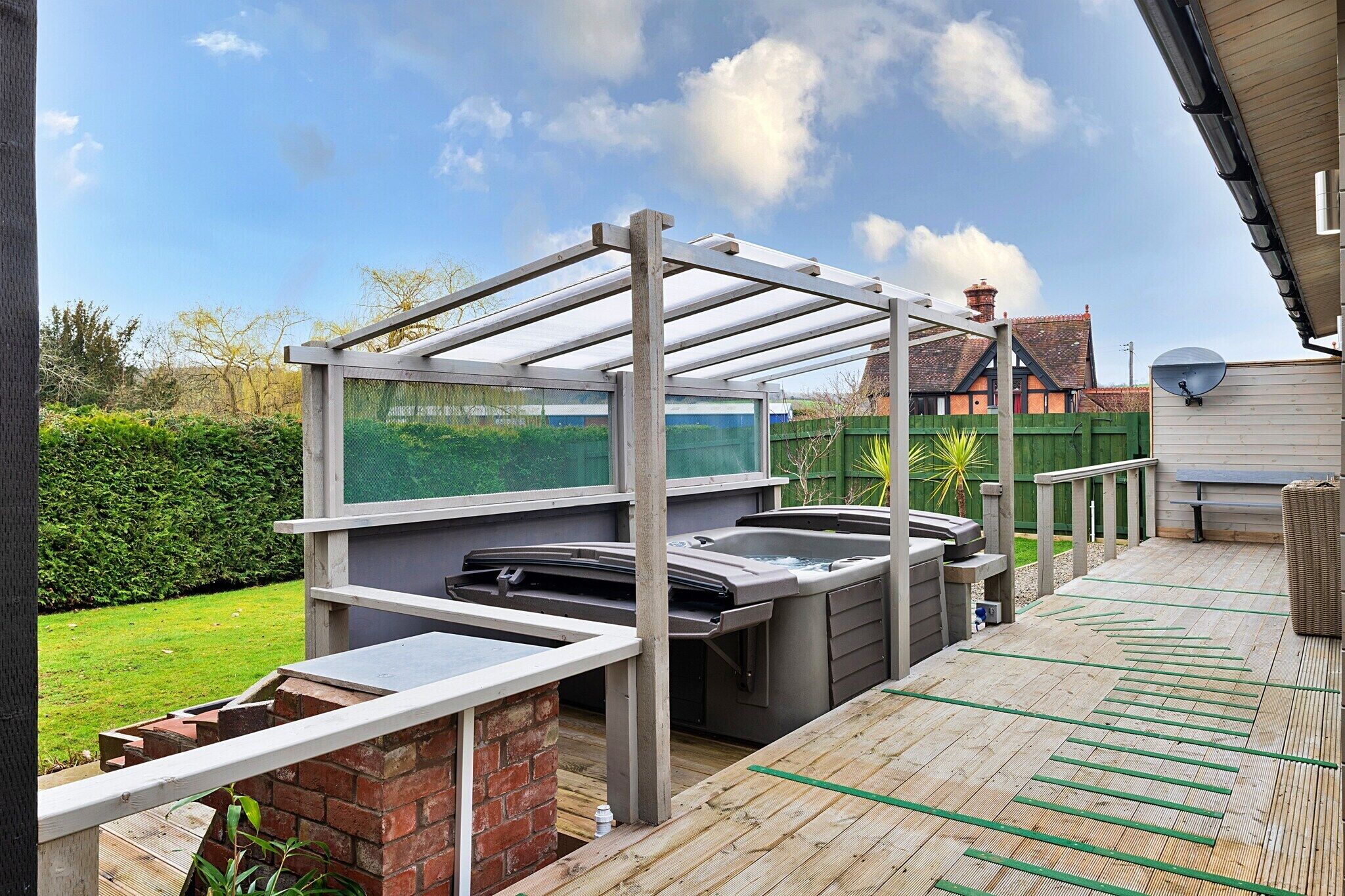 Un espace extérieur abrité avec un jacuzzi, une pergola, un mur en briques et une terrasse en bois.