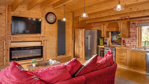 Interior acogedor de una cabaña de troncos con chimenea, muebles de madera y zona de cocina.