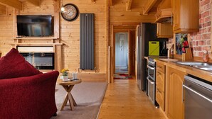 Un interior de madera con televisor, chimenea, cocina y una silla roja.