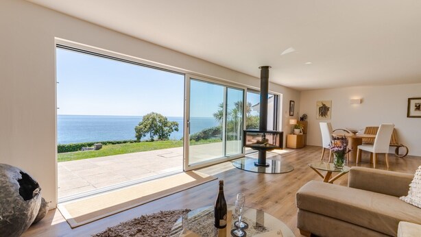 A spacious living area with a large glass door leading to a balcony overlooking the sea.