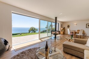 A spacious living area with a large glass door leading to a balcony overlooking the sea. - Chic Coastal Retreat in Downderry with Sea Views (Downderry)