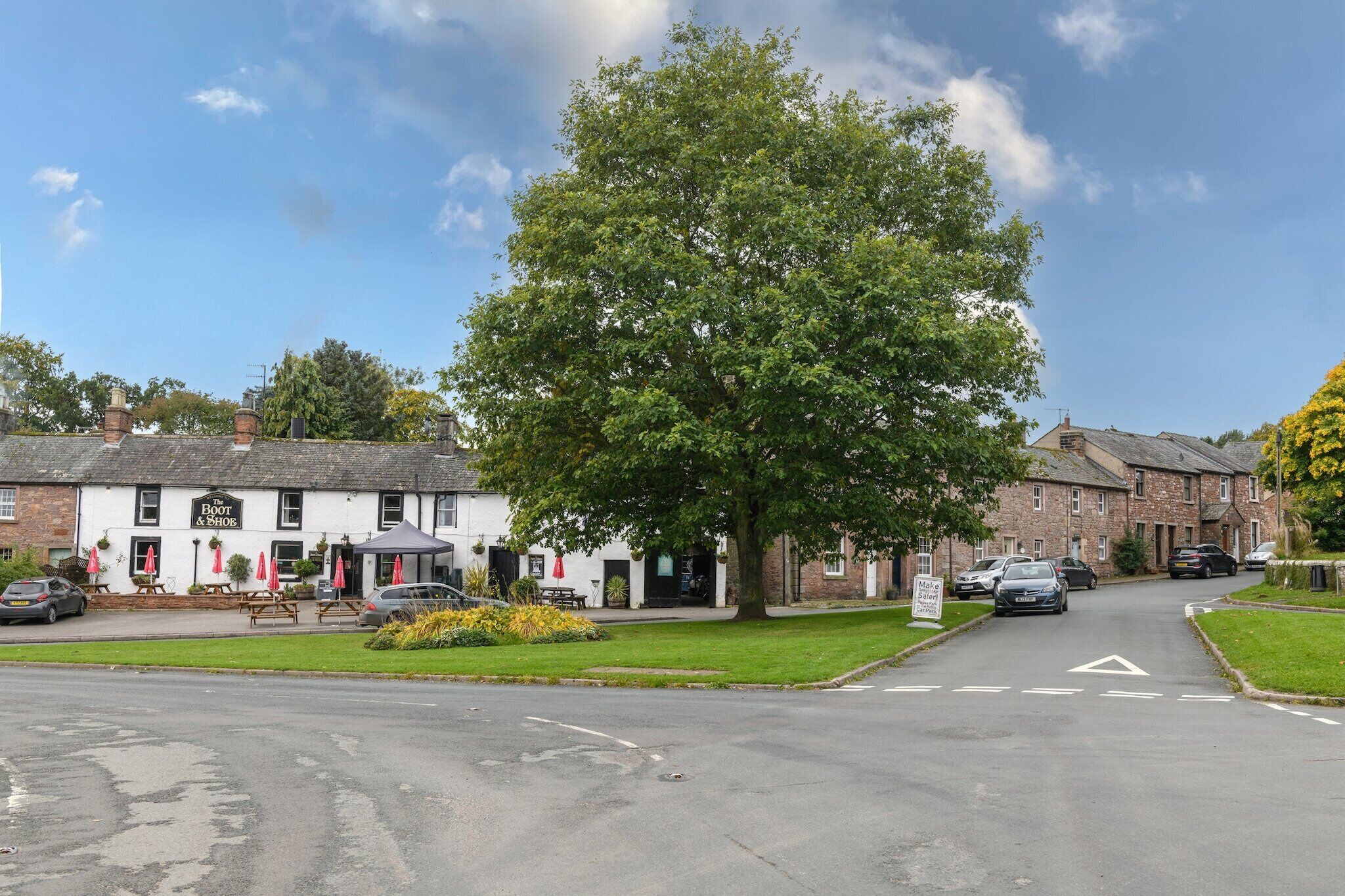 A pub named 'The Boot & Shoe' with outdoor seating, a large tree in front, and a clear road in the background.