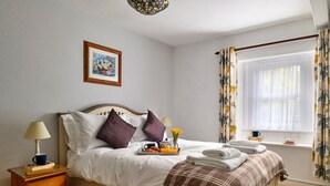 Un lit bien fait, avec des oreillers, une table de chevet avec une lampe, un plateau avec des éléments pour le petit-déjeuner et une fenêtre avec des rideaux.