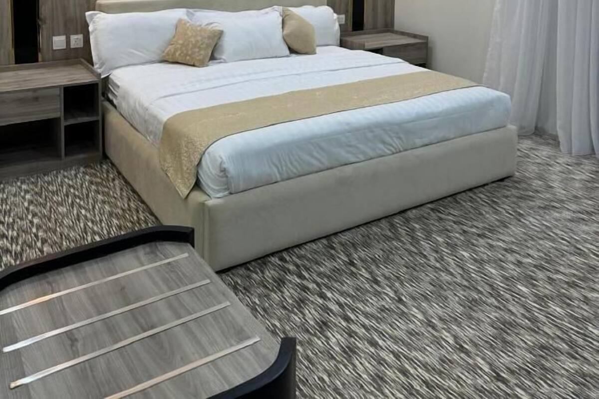 A modern hotel room with a large bed, a round table, and a decorative wall panel.