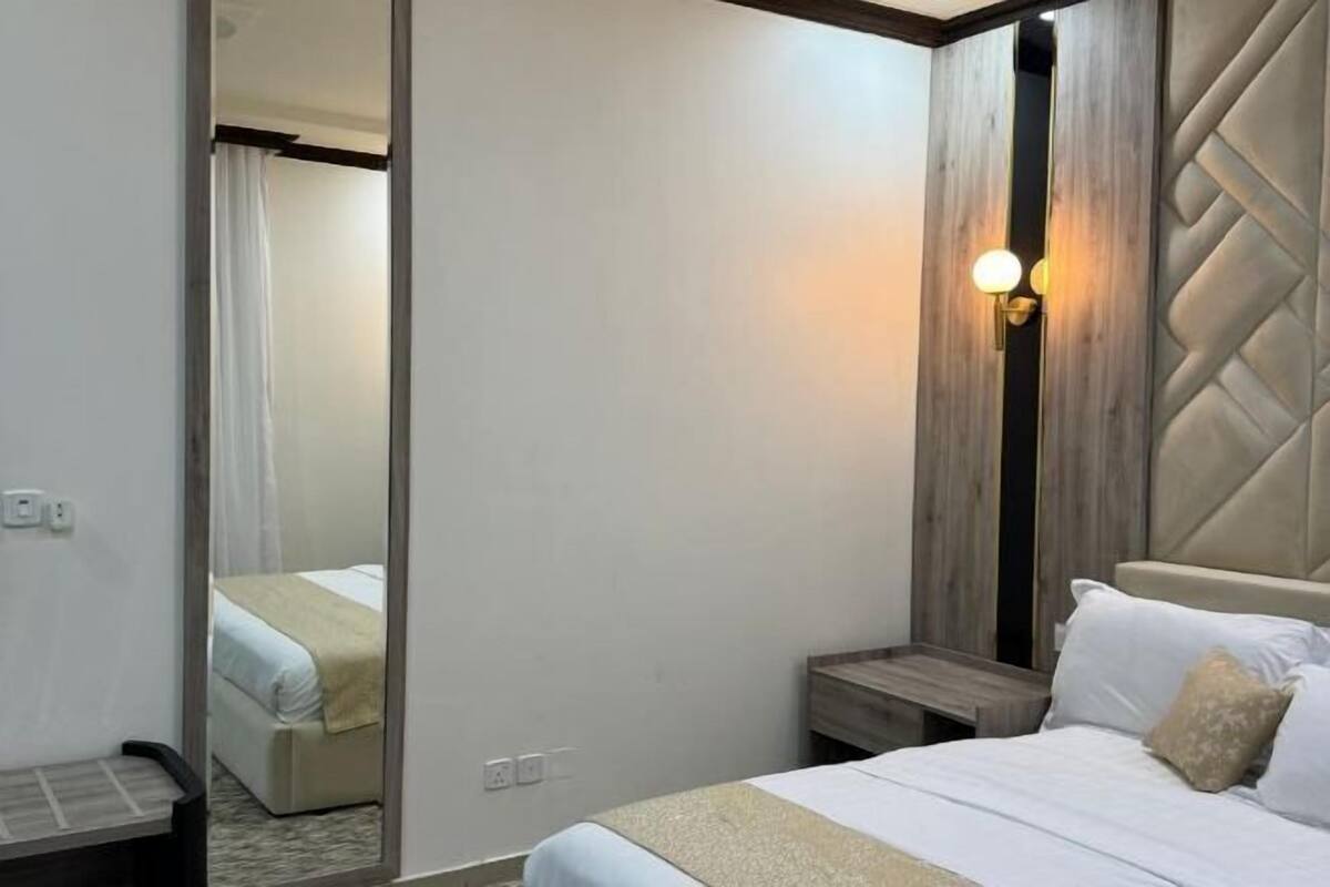 A hotel room with a bed, bedside table, wall-mounted light, and a mirror.