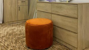 Una camera da letto con un'armadio in legno, uno specchio rotondo e un poggiapiedi arancione.