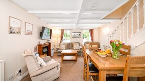 A cozy living room with a sofa, a wooden dining table with chairs, a TV, and a fireplace.