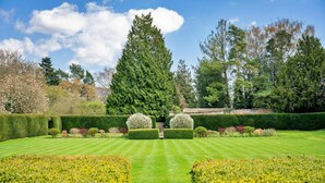 A well-manicured garden with a central pathway, neatly trimmed hedges, and a variety of trees.