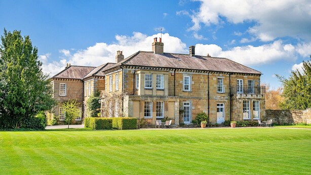 A large, historic stone building with multiple windows and a well-maintained lawn in front.