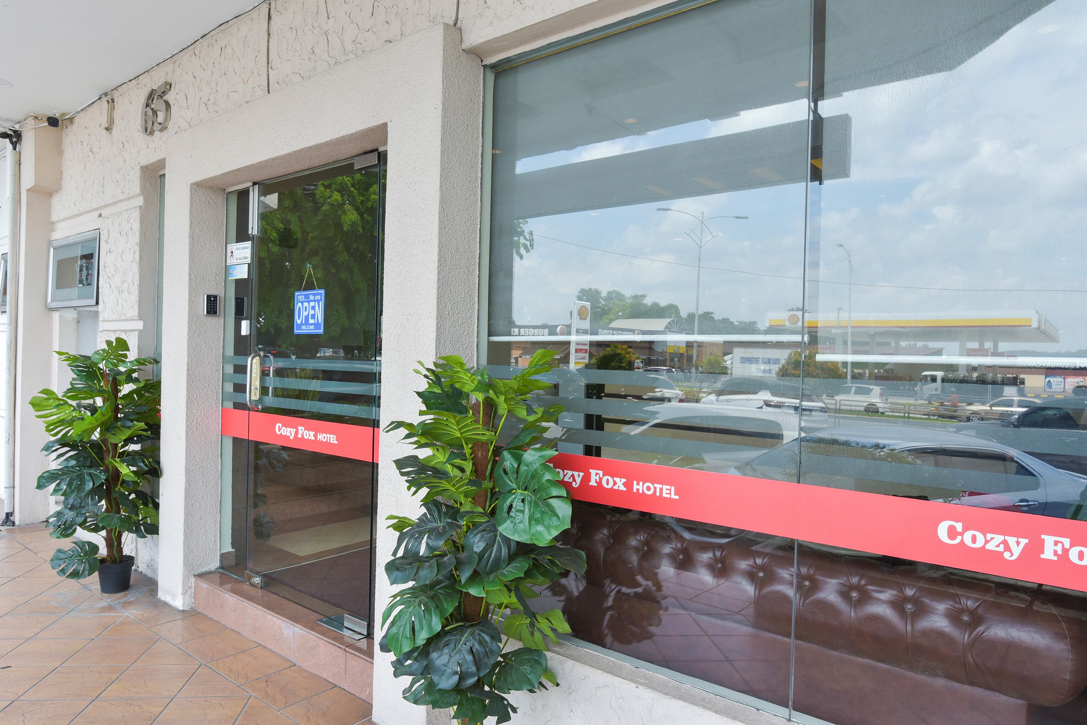 A hotel entrance with a glass door, a sign indicating it's open, and a red banner with the hotel's name.