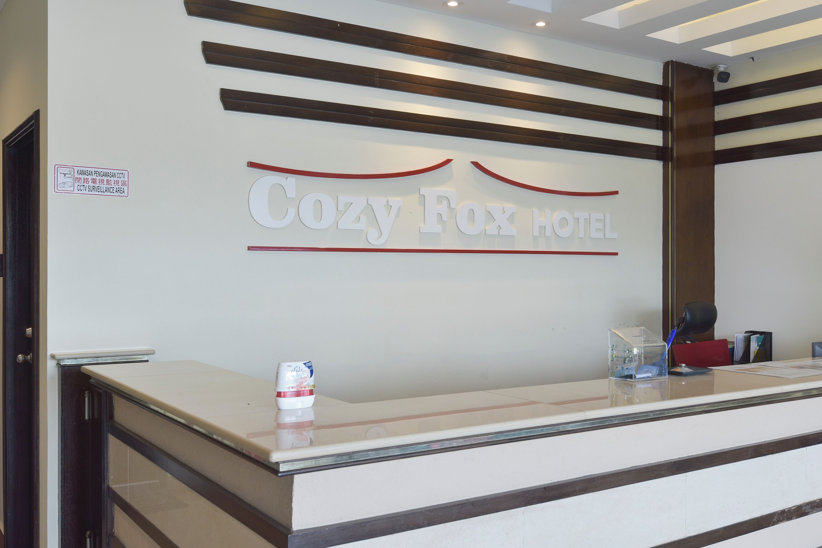 A reception desk with a sign reading "Cozy Fox Hotel" and a CCTV surveillance sign.