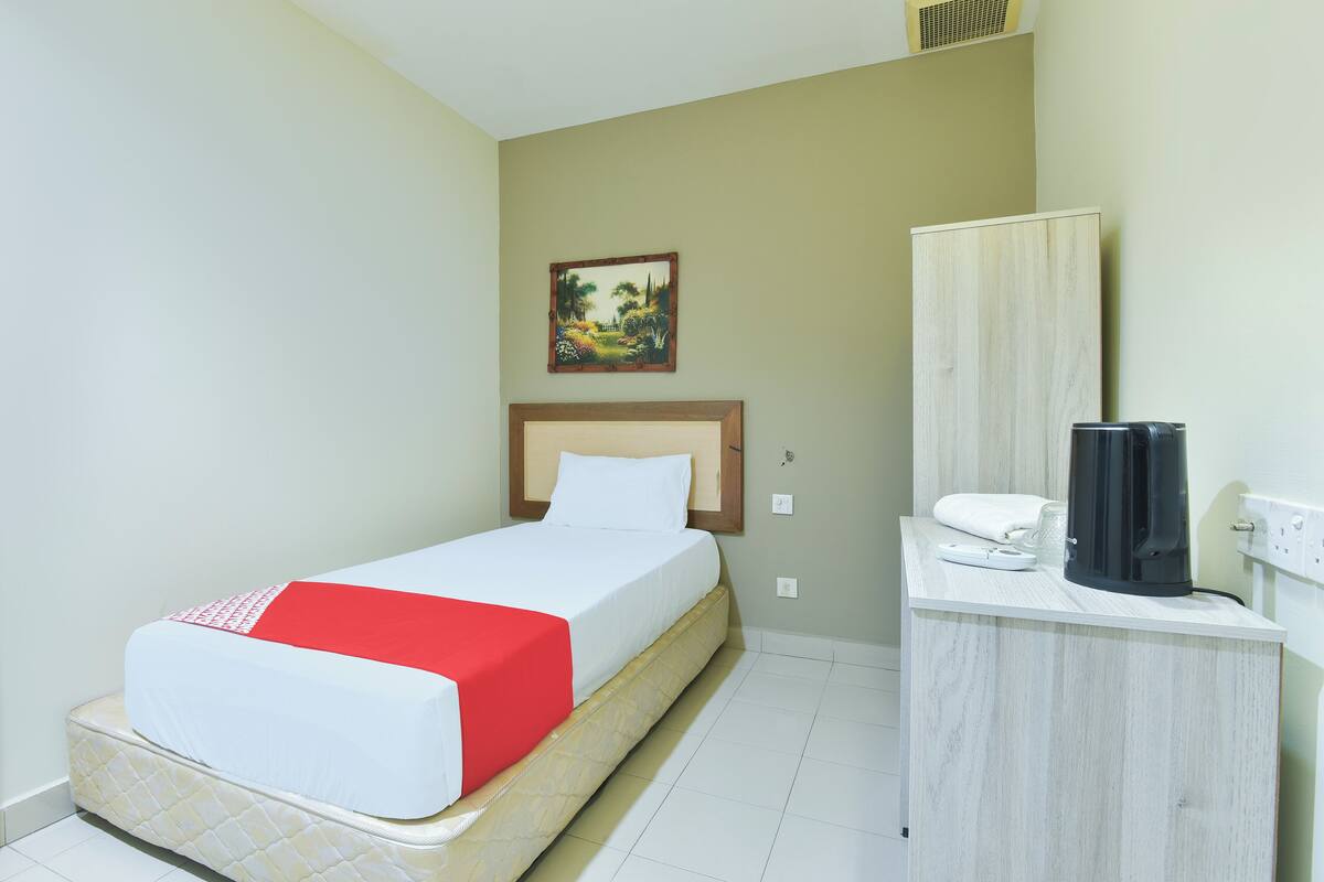 A hotel room with a bed, a bedside table with a phone and a coffee maker, a painting on the wall, and a wardrobe.
