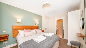 A neatly made bed with pillows, a bedside table, a bench, and a wall-mounted mirror. - Cottage in Thirsk with Scenic Trails & Spa (Thirsk)