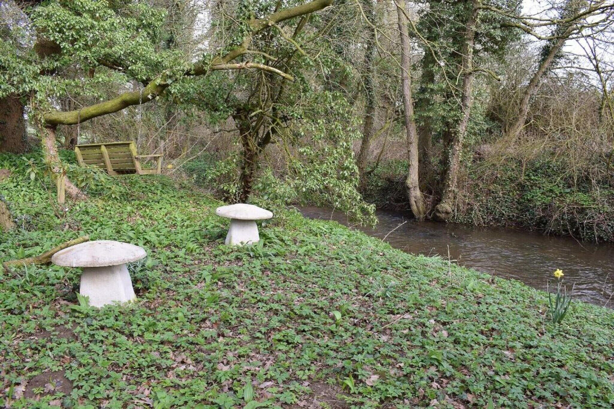 A garden with two mushroom-shaped tables and a wooden bench near a water body.