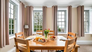 Een eethoek met een houten tafel, gedekt voor het ontbijt, inclusief een fruitschaal, een dienblad met jus d'orange en een vaas met bloemen.