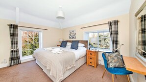A bedroom with a bed, bedside table, chair, and windows.