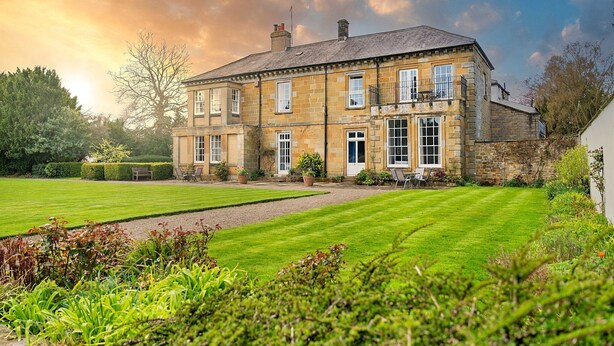 A large stone building with multiple windows and a well-maintained lawn in front.