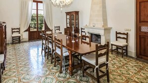 Ein Esszimmer mit einem großen Holztisch, Stühlen, einer Chandelier, einem Kamin und Fliesen mit Muster.
