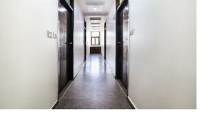 En lång, smal hall med dörrar på båda sidor som leder in till rum. Golvet är kaklat och väggarna är vitmålade.