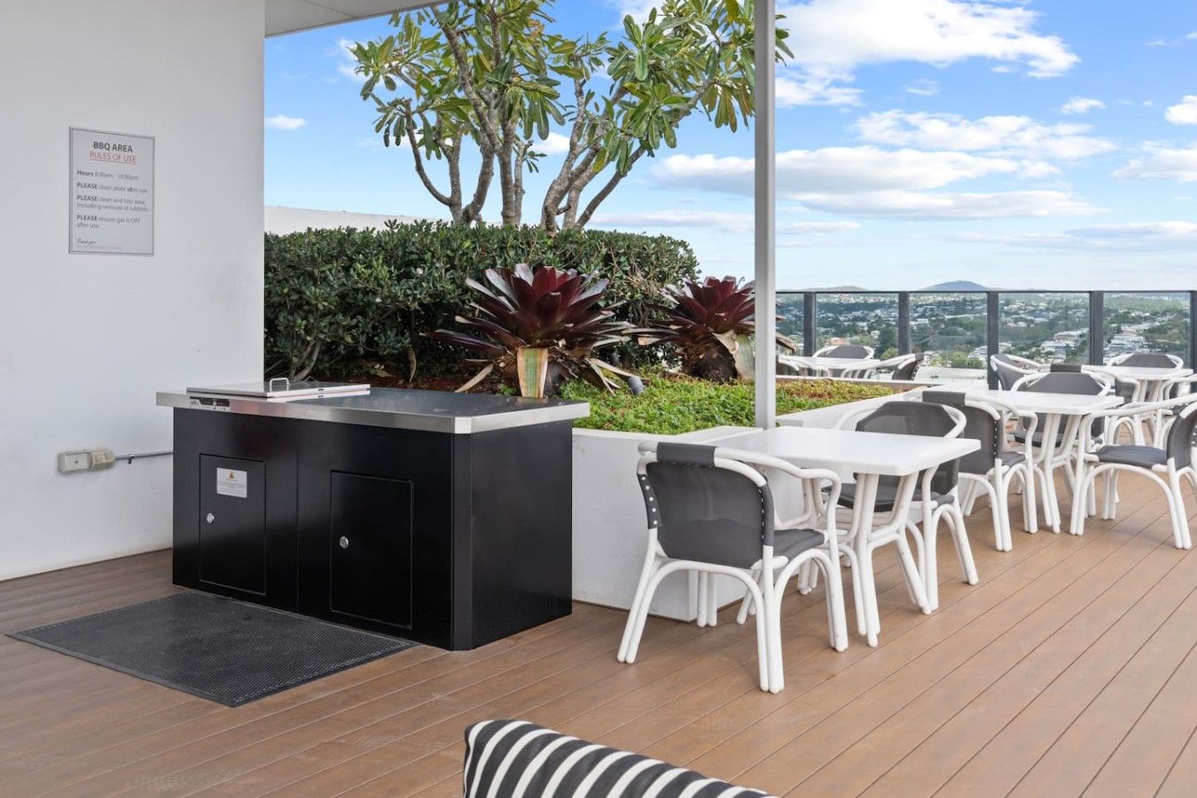 An outdoor seating area with a BBQ station, white chairs, and a view of the city.