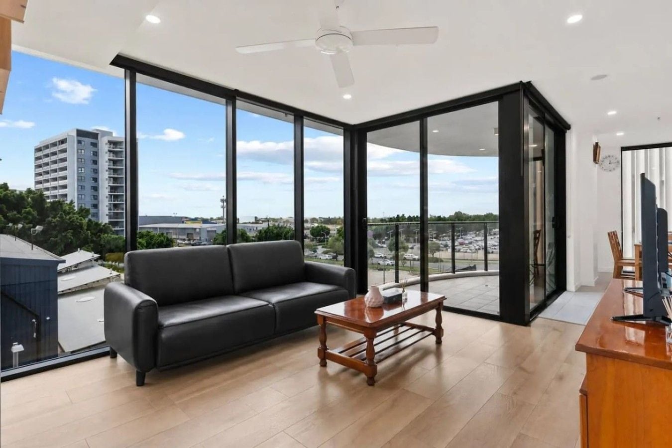 A modern living room with a black leather sofa, a wooden coffee table, and a view of the city through large windows.