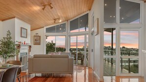 Amplia sala de estar con un ventanal que ofrece vista a la ciudad, techo de madera y comedor con mesa y sillas.