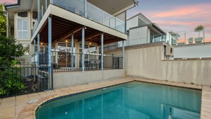 Una casa moderna con piscina, un espacio exterior cubierto y vistas al atardecer.