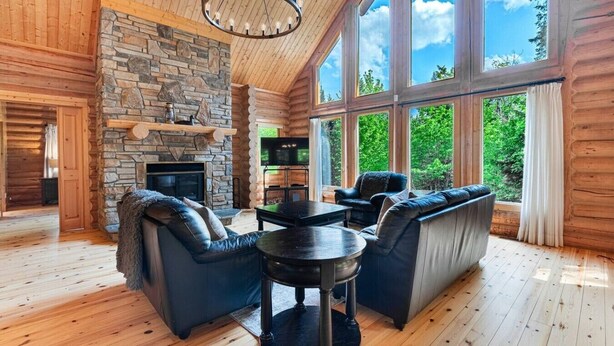 Interior de una cabaña de madera con chimenea de piedra, un televisor y una zona de estar con una mesa y sillas.