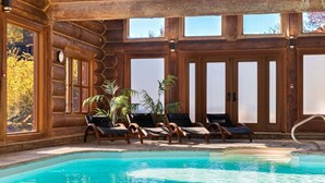 Un área de piscina con paredes de madera, ventanas amplias y sillas de descanso.