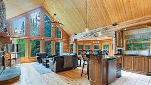 Una cabaña espaciosa con una amplia sala de estar, pisos de madera y una cocina con vista al bosque.