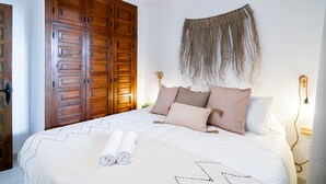 Une chambre avec une grande armoire en bois, un lit avec des serviettes blanches pliées et un luminaire fixé au mur.