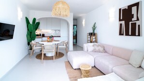 Un salon moderne avec un canapé, un coin repas comprenant une table et des chaises, et une cuisine en arrière-plan.