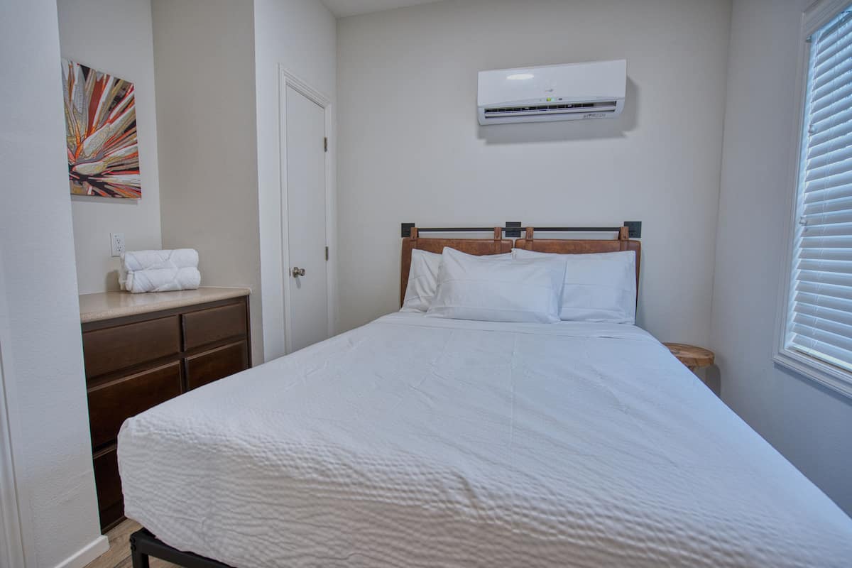 Un dormitorio con cama, cómoda, aire acondicionado y ventana con persianas.