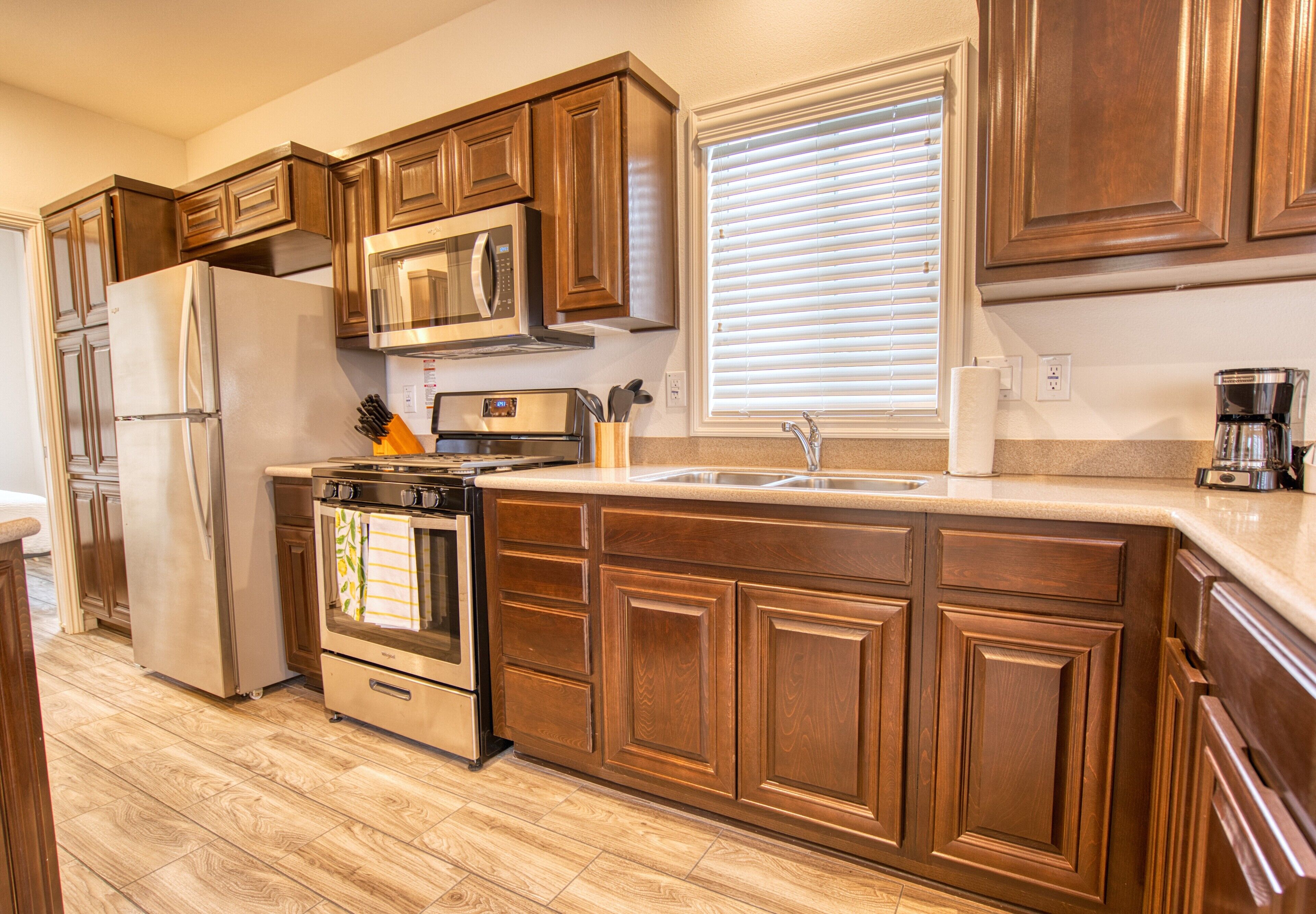 A kitchen with wooden cabinets, stainless steel appliances, and a window with blinds.