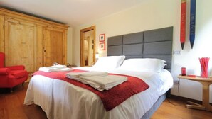 A hotel room with a large bed, a red armchair, wooden wardrobe, and two large pencils on the wall. - Apartment in a chalet nestled in the forest, with sauna and private forest (Canal San Bovo)