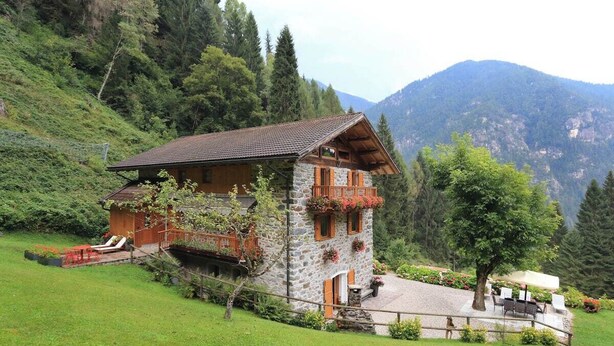 A stone chalet with a balcony, surrounded by lush greenery and mountains. - Apartment in a chalet nestled in the forest, with sauna and private forest (Canal San Bovo)