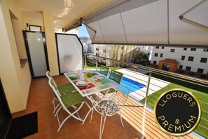 A balcony with a table set for dining, a chair, and a view of a swimming pool and buildings.