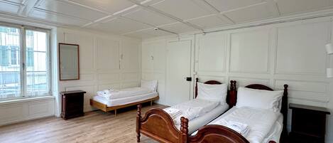 A bedroom with a wooden bed, a small bedside table, a mirror, and a window with a view.