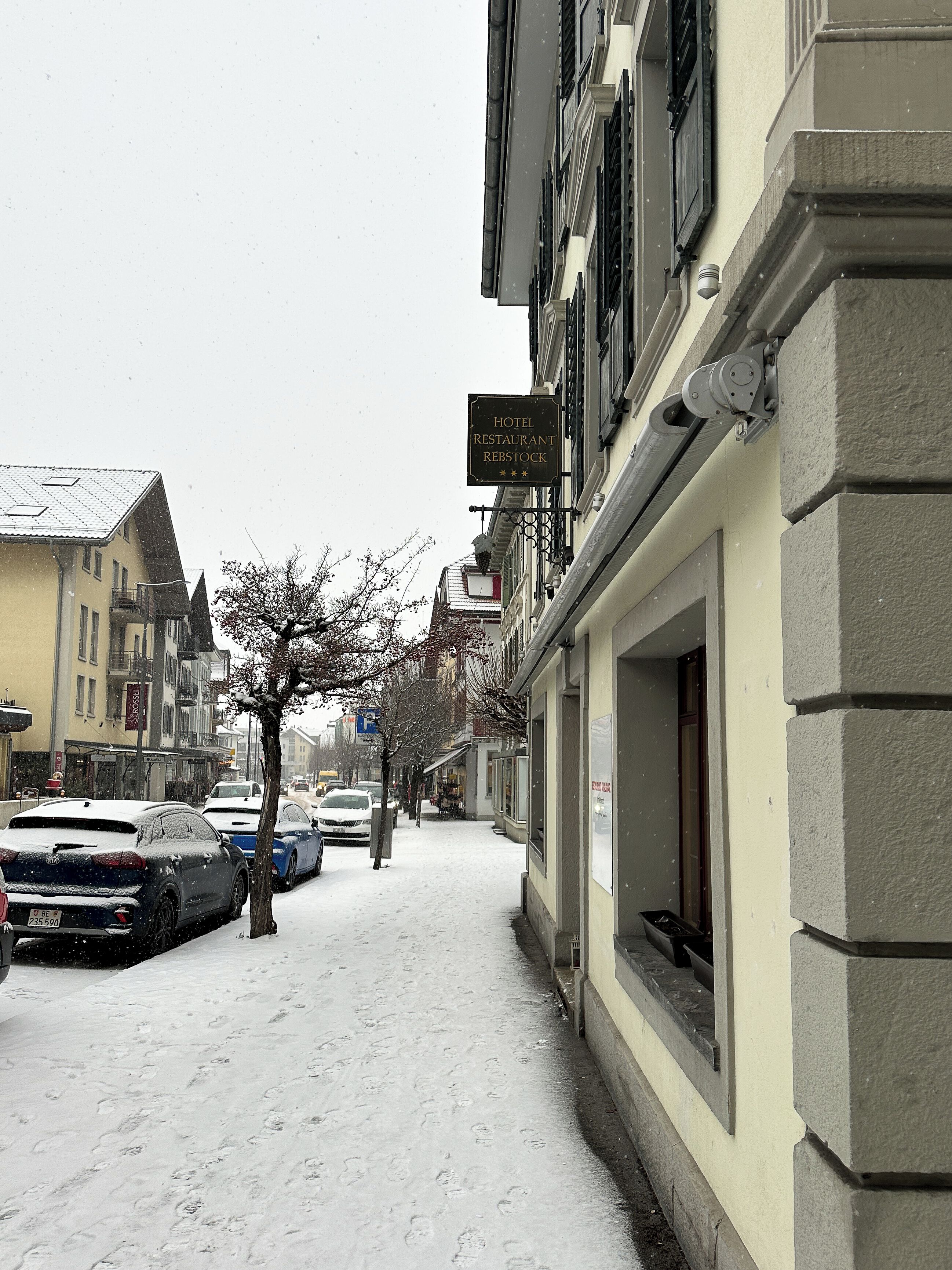 Un letrero de hotel con clasificación de cuatro estrellas, una acera cubierta de nieve, coches estacionados y edificios de arquitectura tradicional.