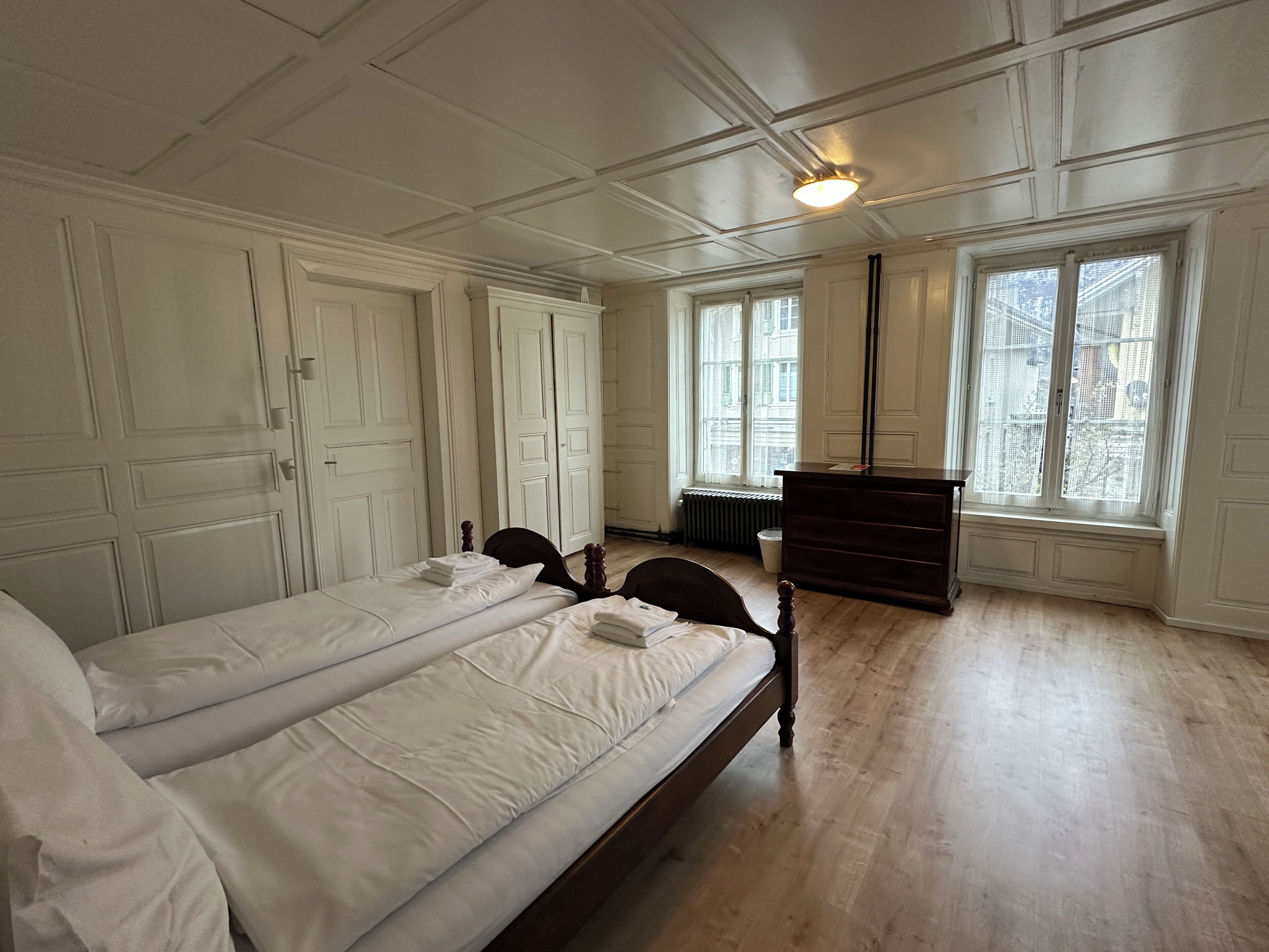 Una habitación con dos camas, un aparador y ventanas amplias.