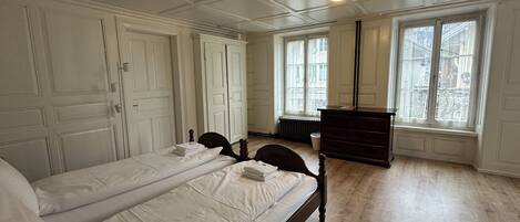 Una habitación con dos camas, un aparador y ventanas amplias.