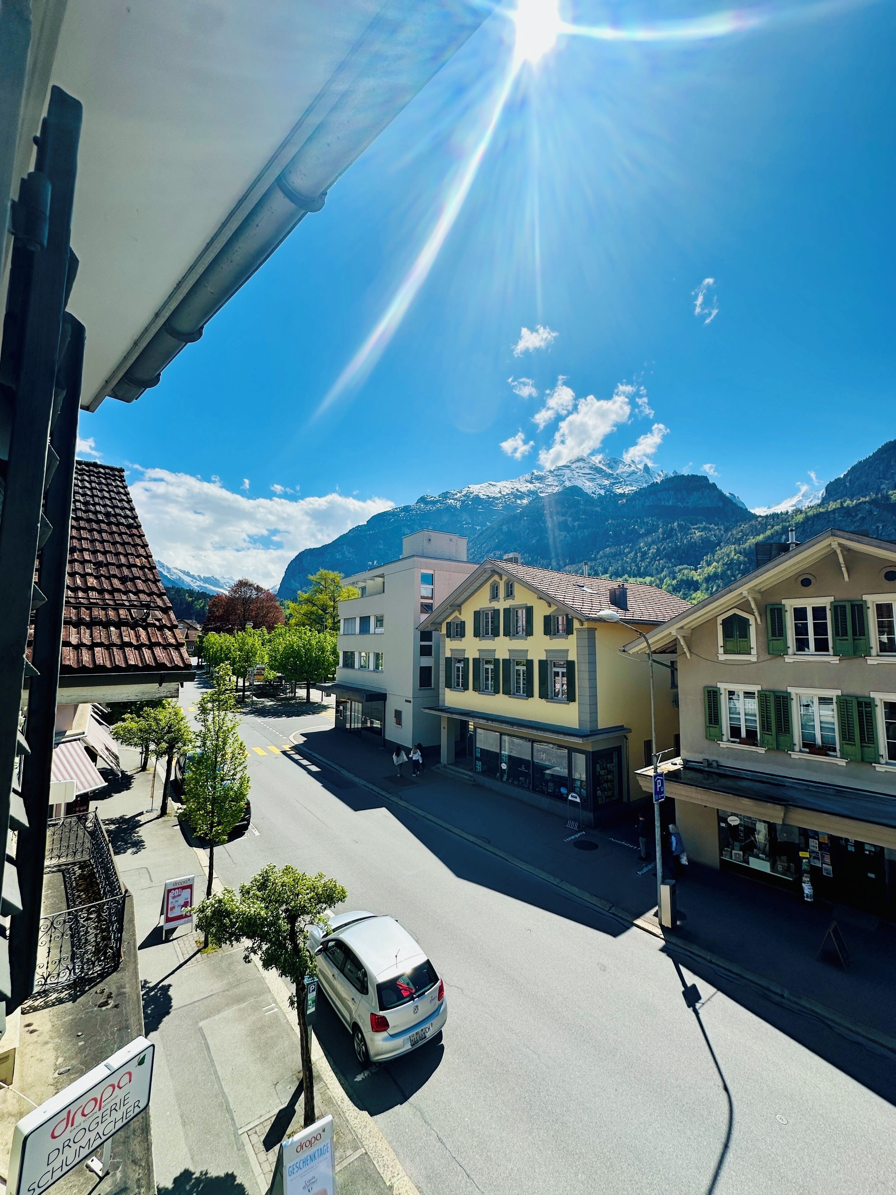A street view with buildings, a parked car, and mountains in the background.