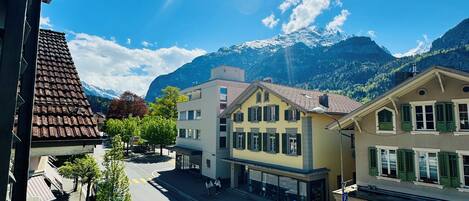 A street view with buildings, a parked car, and mountains in the background.